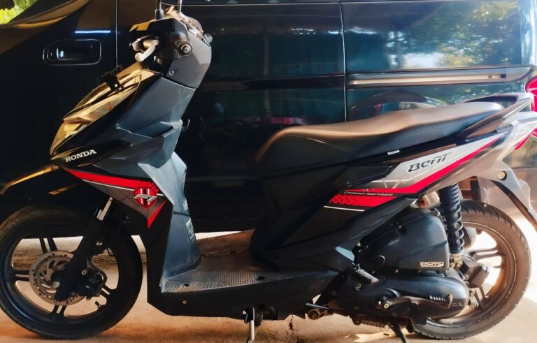 Motor skuter Honda Beat berwarna hitam dengan aksen merah, dilengkapi mesin efisien dan desain modern, cocok untuk penggunaan sehari-hari.