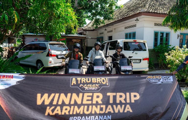 Tiga pengendara sepeda motor NMAX Turbo berdiri di depan spanduk pemenang trip Karimunjawa, dengan kendaraan di latar belakang.